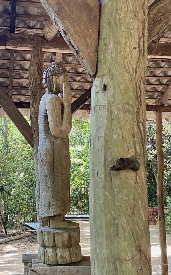 A carved standing Buddha beside a timber post
